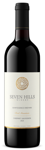 A bottle of Seven Hills Winery red wine with a cream label displaying the winerys name, a gold circular emblem, and text indicating it is a 2021 Quintessence Vineyard Cabernet Sauvignon.