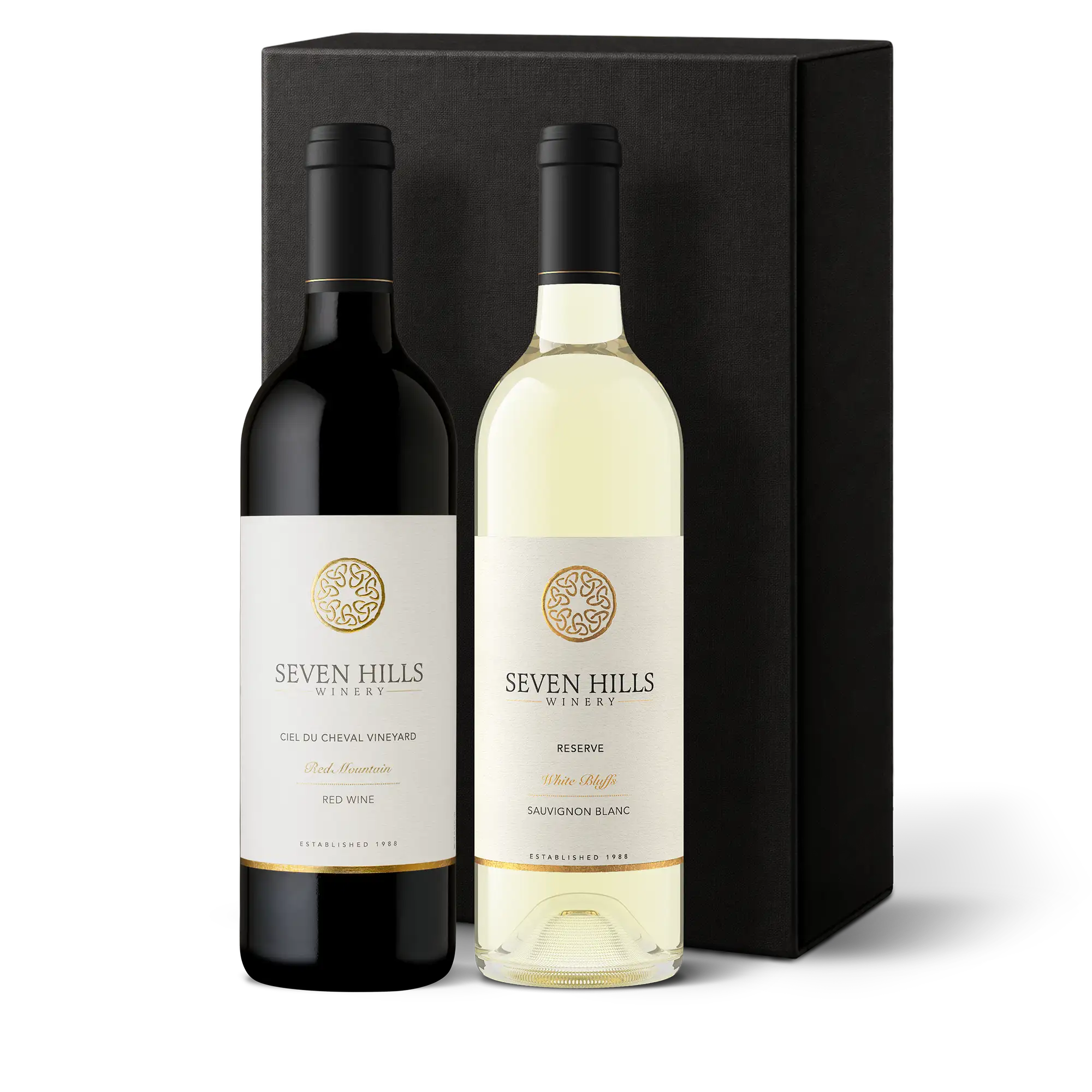 Two bottles of Seven Hills Winery—Washington’s Finest Wine—one red, one white—stand in front of a black gift box. The labels feature a gold emblem and text identifying the wines and vineyard, making this a distinguished Wine Gift for any occasion.
