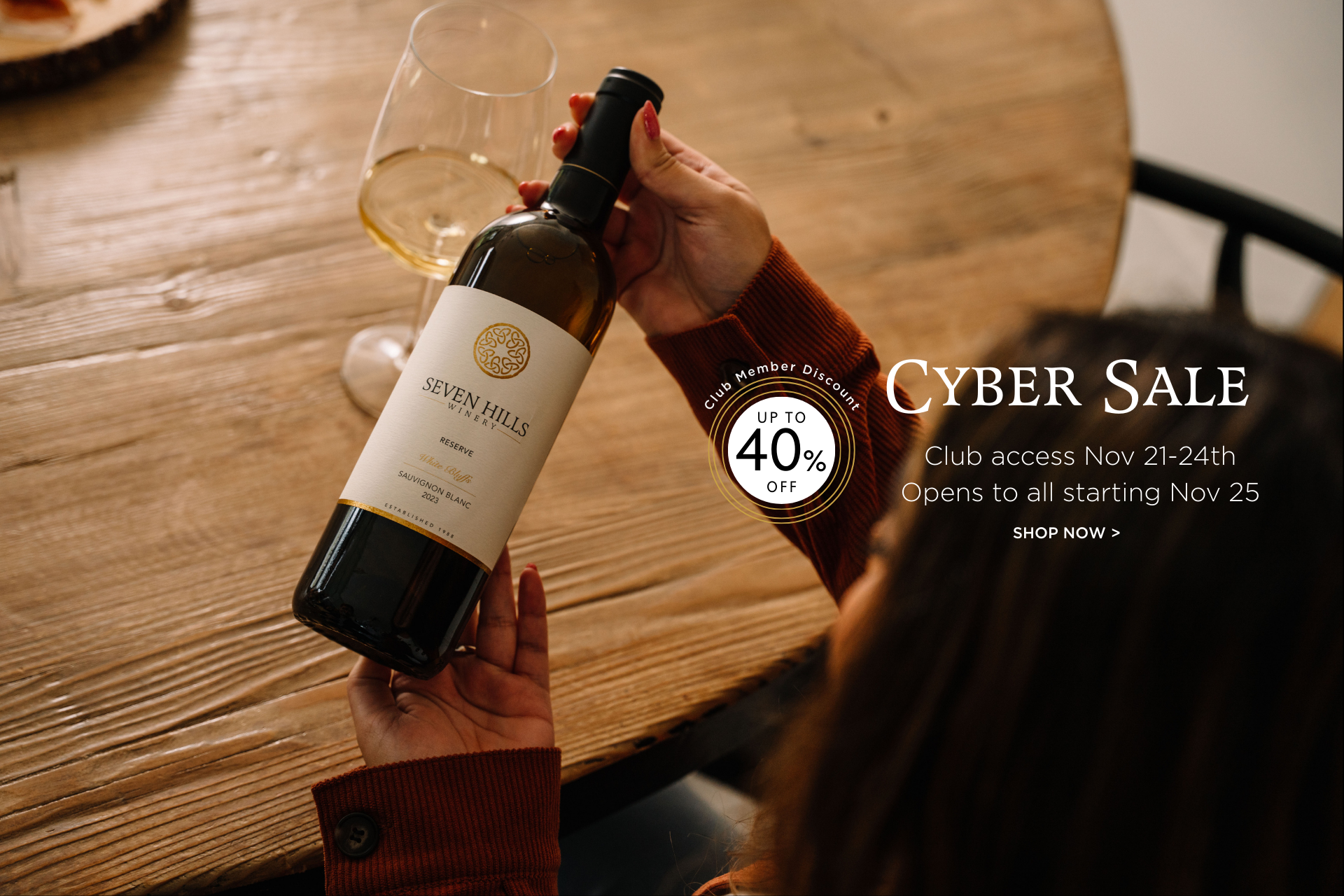 A person holds a bottle of Seven Hills wine next to a filled wine glass on a wooden table. Text on the image promotes a Cyber Sale with up to 40% off from Nov 21–24 and public access starting Nov 25.