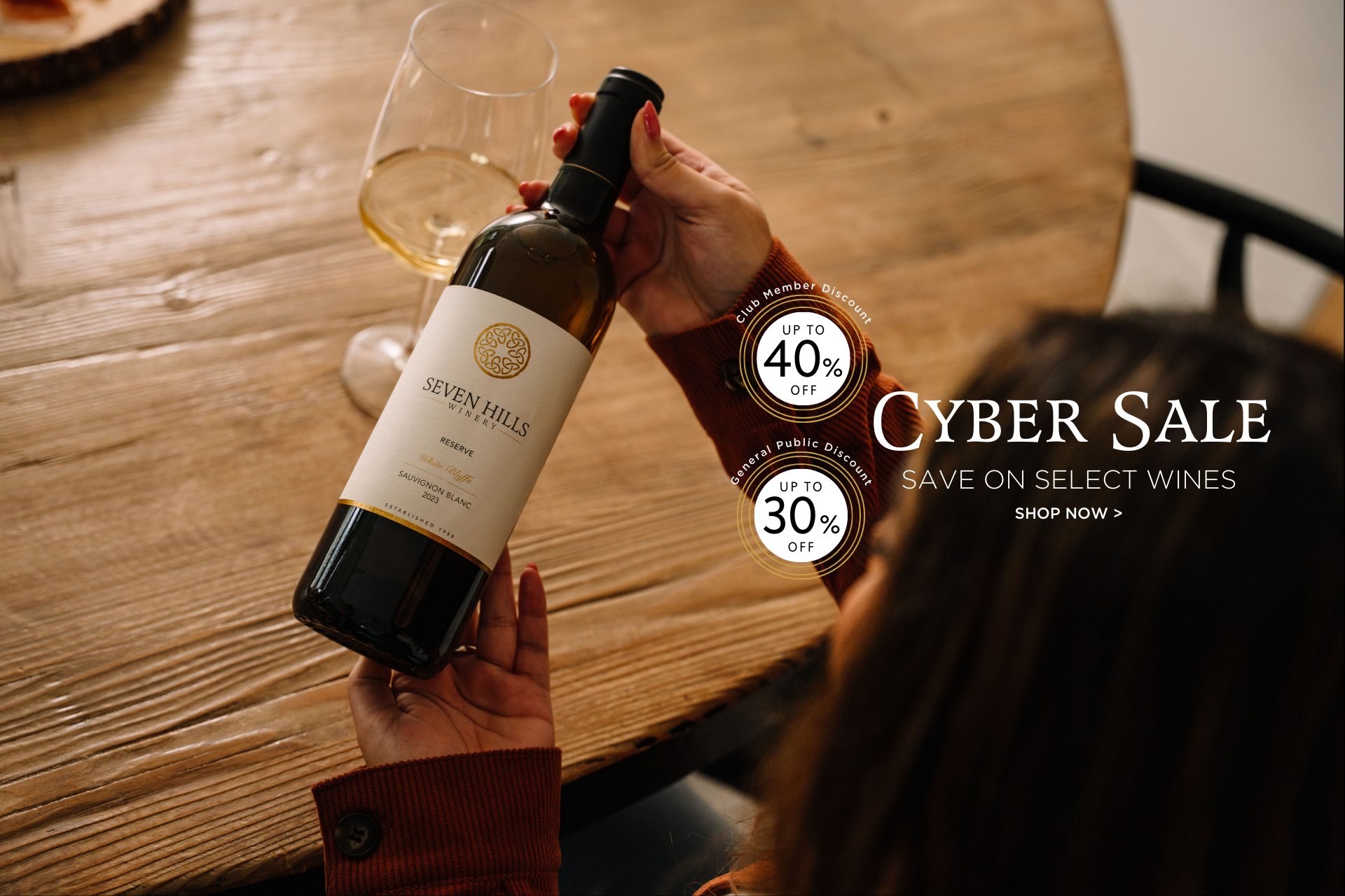 A person holds a bottle of Seven Hills wine at a table with a glass of white wine. Text reads Cyber Sale, Save on Select Wines, Shop Now with discount badges of up to 40% and 30% off.
