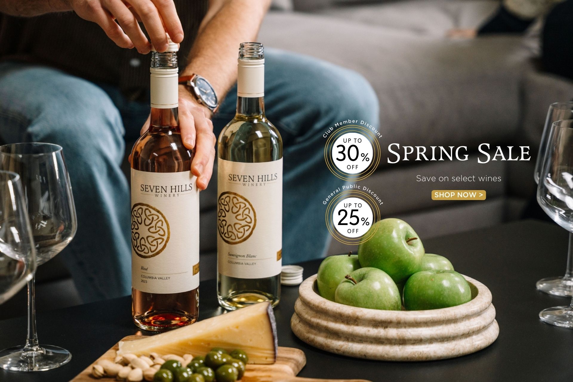 Two hands open bottles of Seven Hills wine near glasses, cheese, olives, and green apples on a table. Text reads: Spring Sale, Save on select wines, Up to 30% off, Up to 25% off, Shop Now.